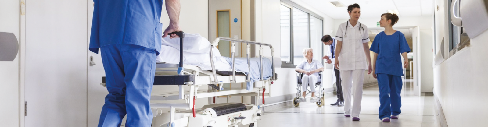 En vit sjukhuskorridor med blå- och vitklädd personal som rör sig i olika riktningar 