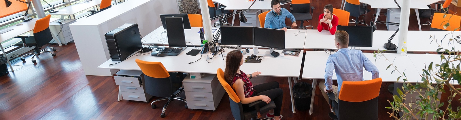 Ett öppet kontorslandskap där fyra affärsklädda människor, två män och två kvinnor sitter och diskuterar. 